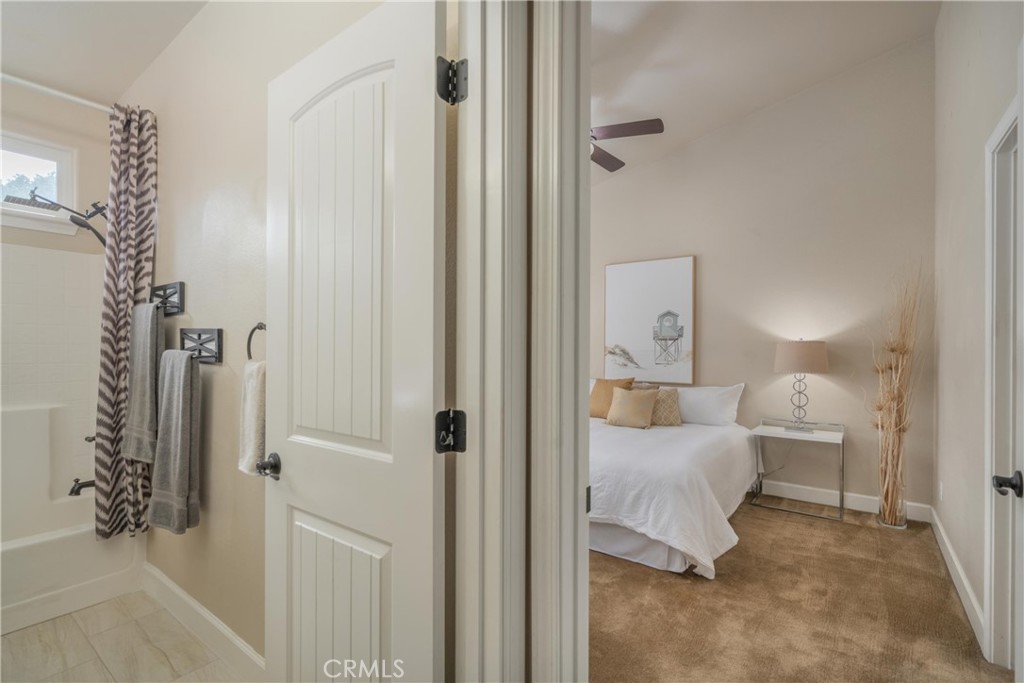 Bedroom with a white bed and tan carpet, viewed beside an adjoining bathroom.
