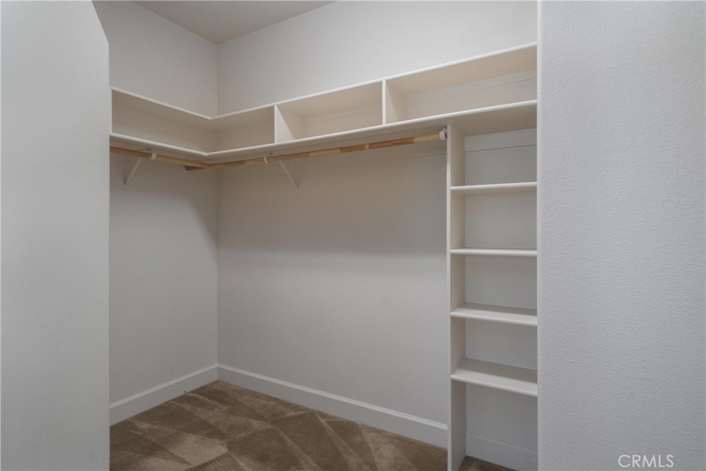 Walk-in closet with upper shelves, a wooden hanging rod, and built-in shelving.