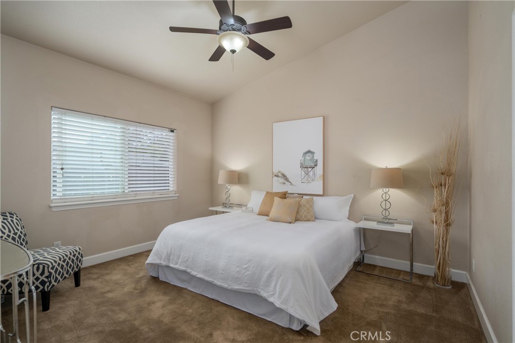 Staged bedroom with a white bed, ceiling fan, and wide window with blinds.