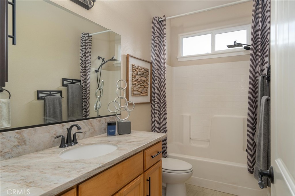 Bathroom with a long wood vanity, stone-look counter, and tub behind a patterned shower curtain.
