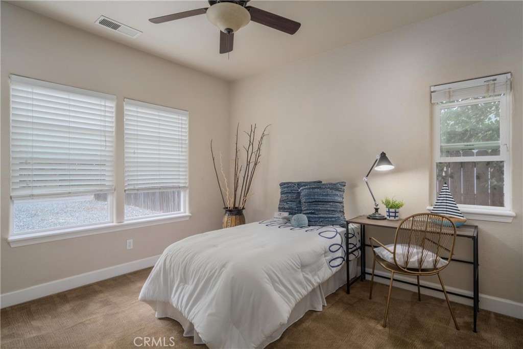 Staged bedroom with a white bed, blue pillows, and a desk beside the window.