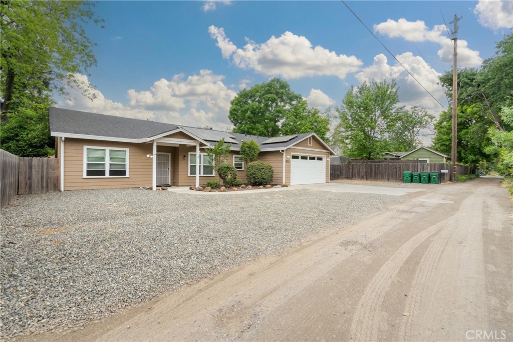 Single-story tan home with an attached garage, covered entry, and broad gravel driveway.