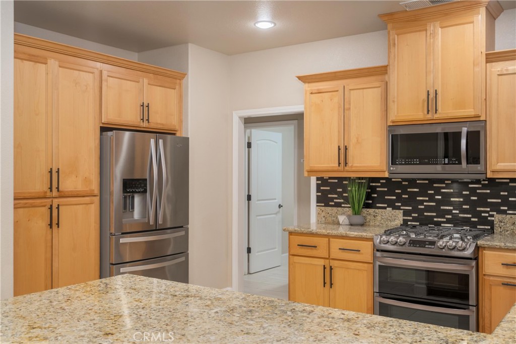 Kitchen with light wood cabinets, granite counters, stainless steel appliances, and a dark tile backsplash.