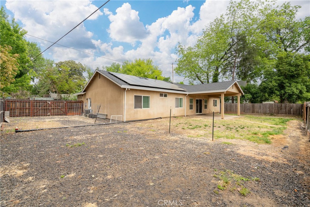 Rear exterior of a single-story home with rooftop solar panels, covered patio, and fenced yard.