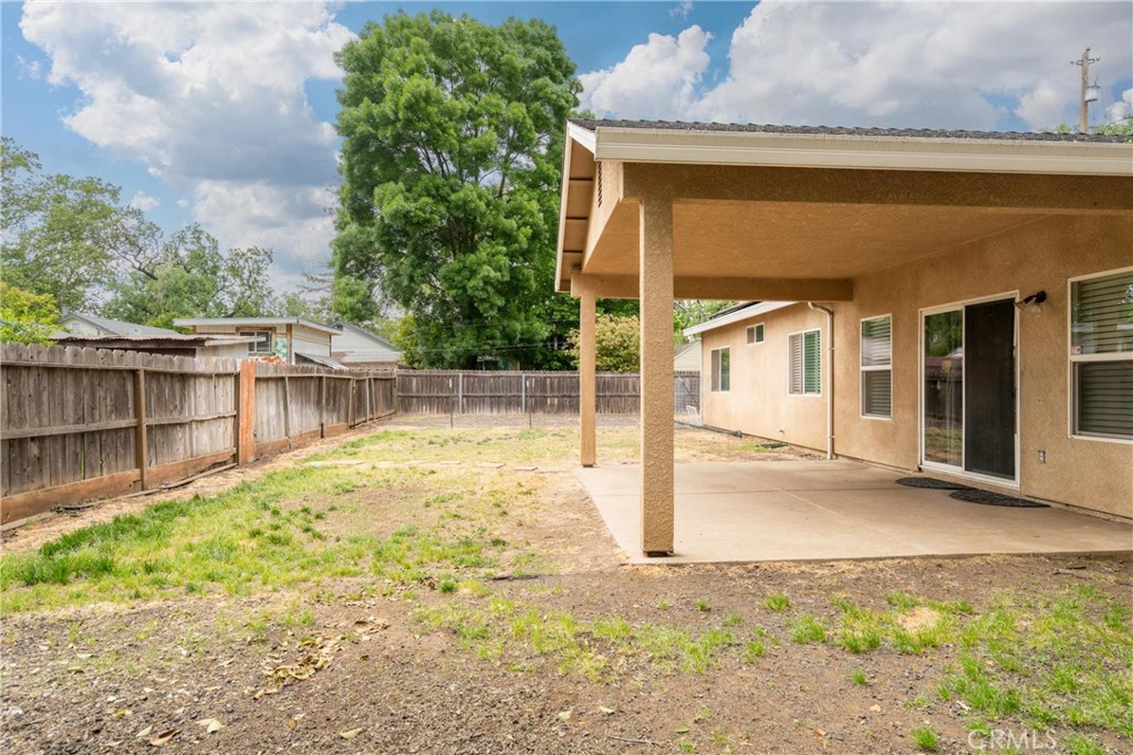 House’s covered rear patio beside a fenced backyard with sparse grass and mature trees.