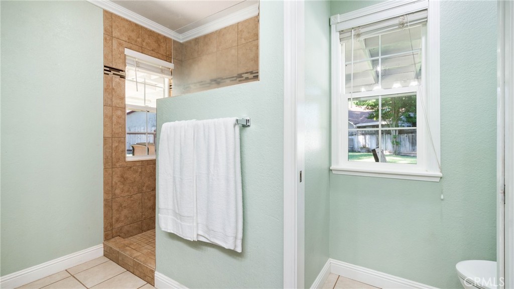 Bathroom with a tan tiled shower, white towel, and window overlooking a fenced yard.