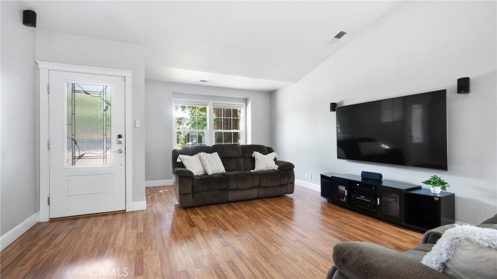 Living room with hardwood floors, a decorative-glass entry door, dark sofa, and wall-mounted television.