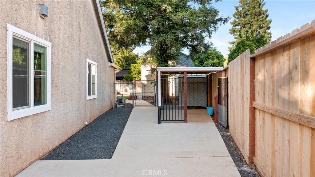 Side yard with a concrete walkway, gated covered area, and tall wooden fence.