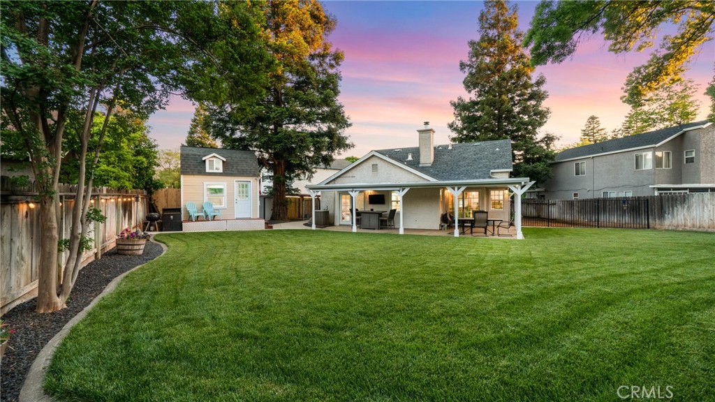 Fenced backyard with a broad lawn, covered patio, and detached shed at sunset.