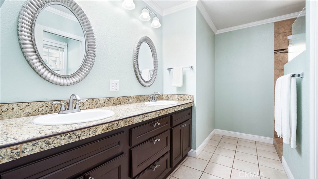 Bathroom with a dark double vanity, speckled stone countertop, and two oval mirrors.