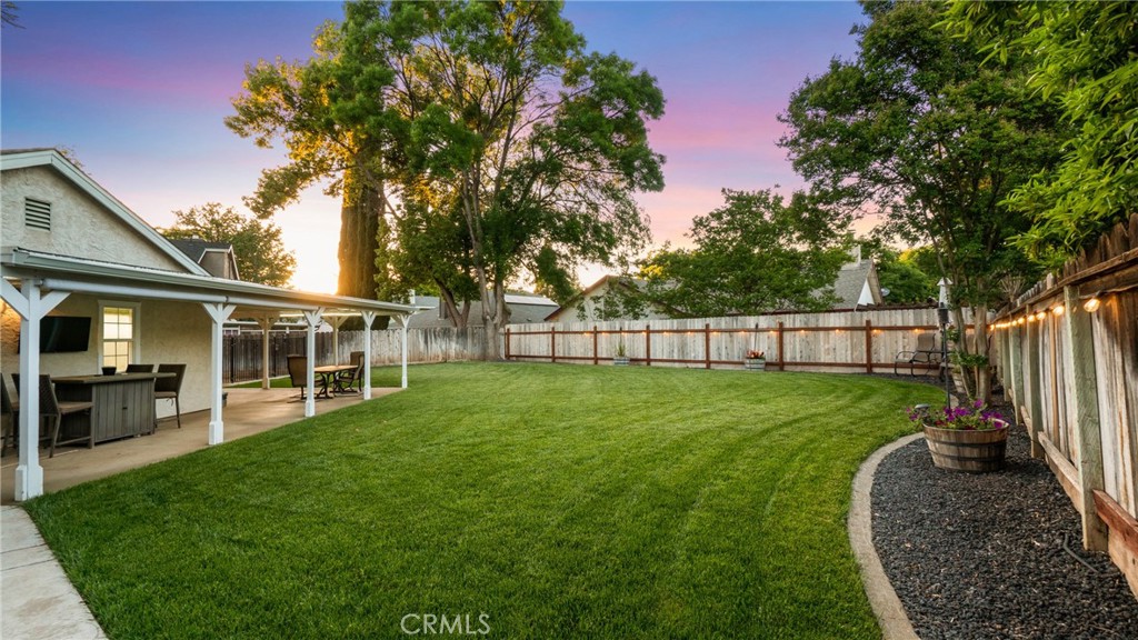 Backyard with a broad lawn, covered patio, mature trees, and string lights along the fence.