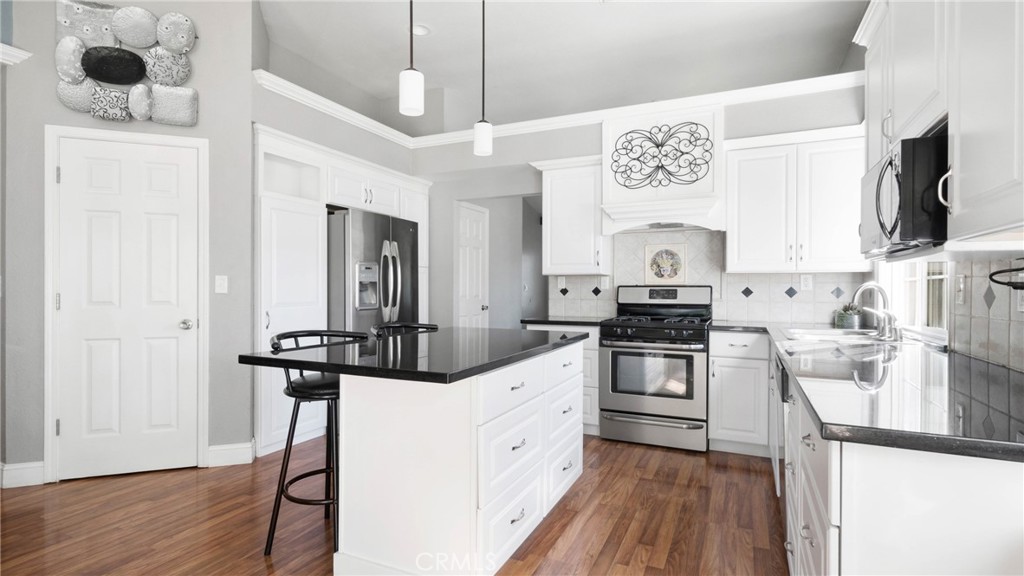 Kitchen with a black-topped island, white cabinetry, stainless steel appliances, and wood flooring.