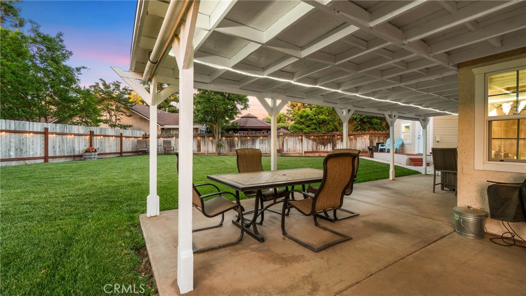 Covered patio with outdoor dining set overlooking a fenced green backyard at dusk.