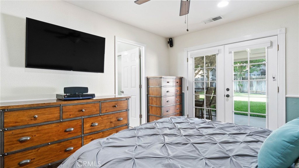Bedroom with a gray tufted bed and glass doors overlooking a grassy yard.