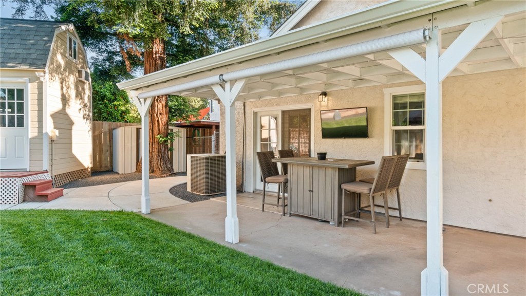 Covered patio with outdoor dining set beside a green lawn and detached outbuilding.