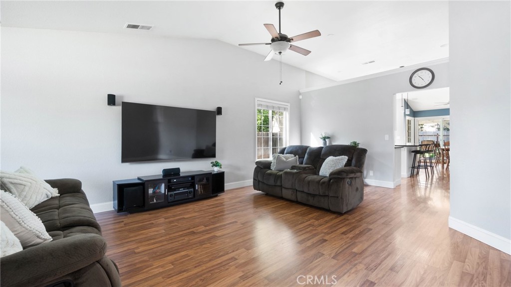 Living room with gray sofas, a wall-mounted television, wood-look floors, and an open view to the dining area.