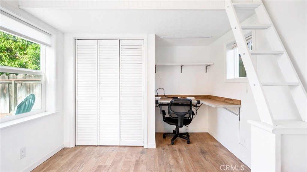 Bright home office nook with a built-in desk, rolling chair, and ladder to an overhead loft.