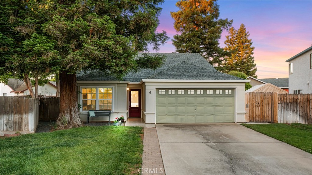 Single-story house with a two-car garage, broad driveway, lawn, and mature trees at dusk.