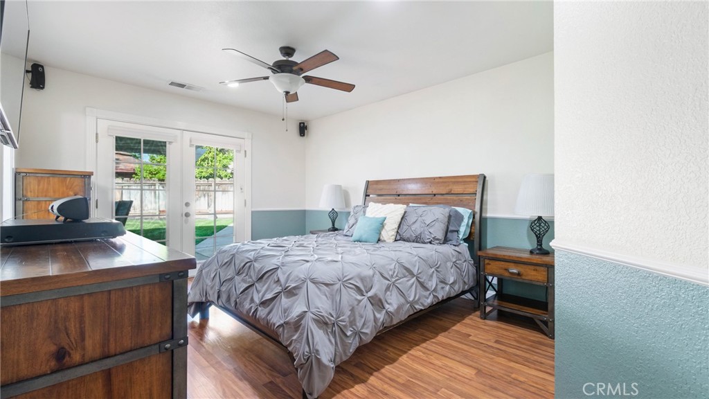 Bedroom with gray patterned bedding and French doors opening to a fenced backyard.