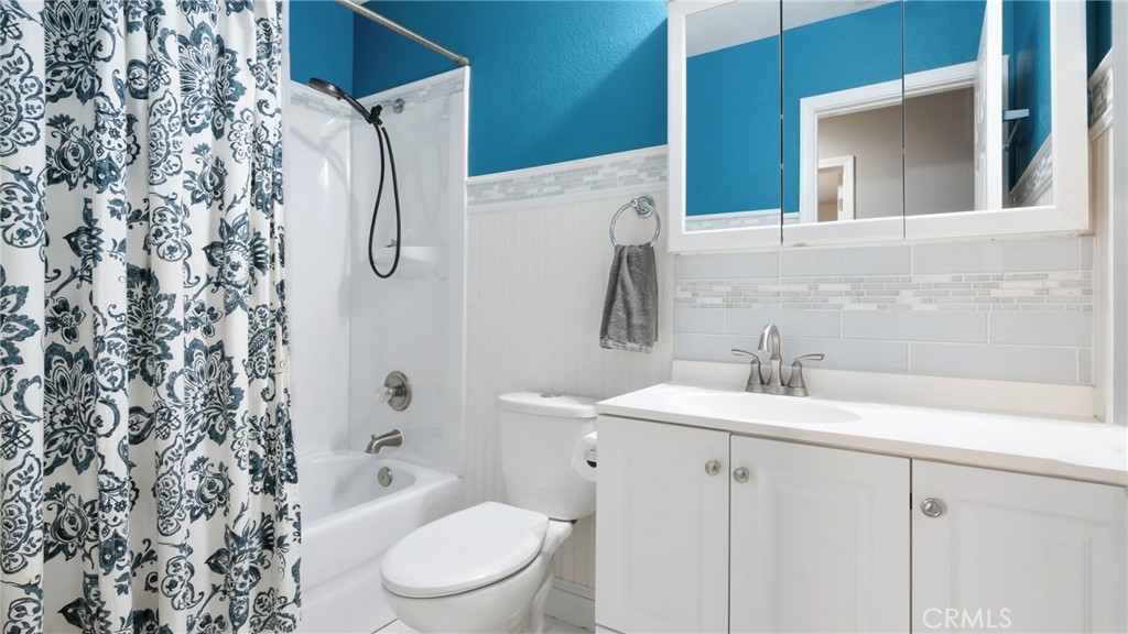 Bathroom with turquoise walls, floral shower curtain, white tub, toilet, and vanity.