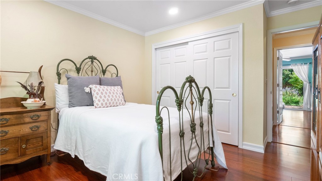 Staged bedroom with an ornate green metal bed, wooden nightstand, and white closet doors.