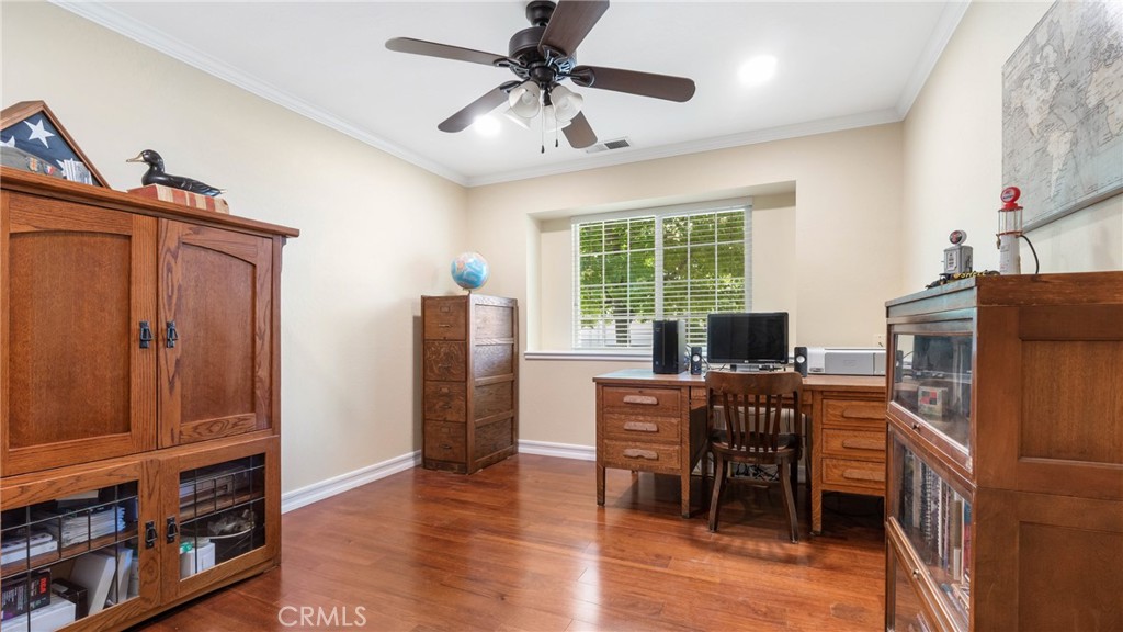 Home office with a wooden desk, matching cabinets, hardwood floors, and a window with blinds.