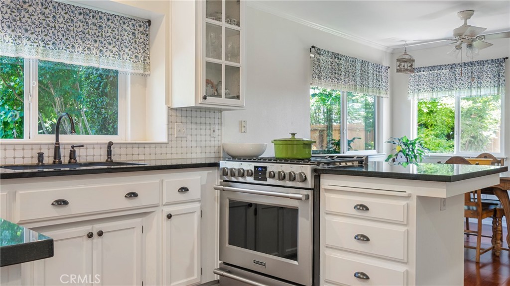 Kitchen with a stainless-steel range, black countertops, and large windows overlooking greenery.