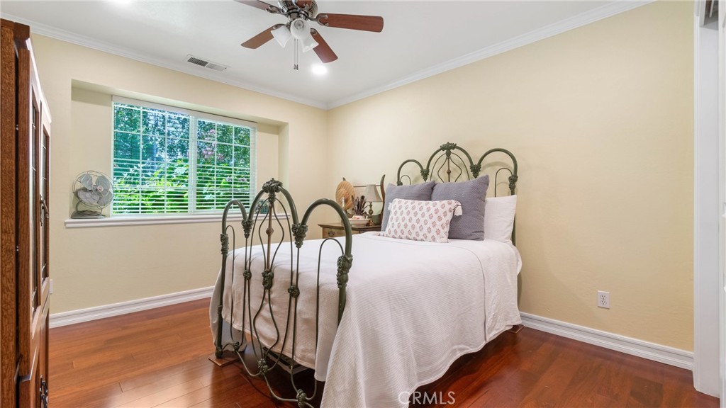 Bedroom with an ornate black metal bed, white bedding, hardwood floors, and a wide window.