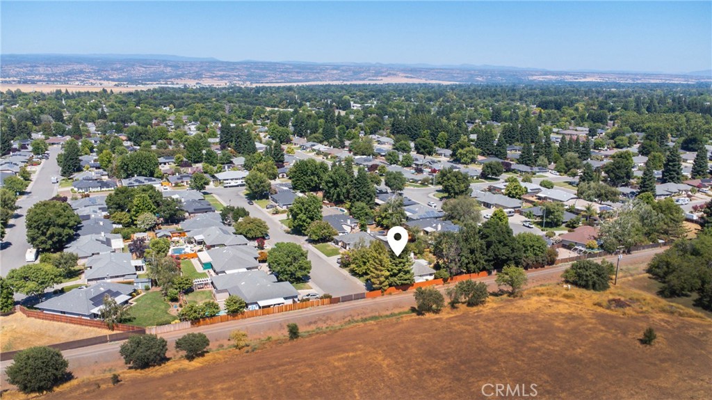 Aerial view of a tree-lined Chico neighborhood beside a dry open field, with a pin marking the property.