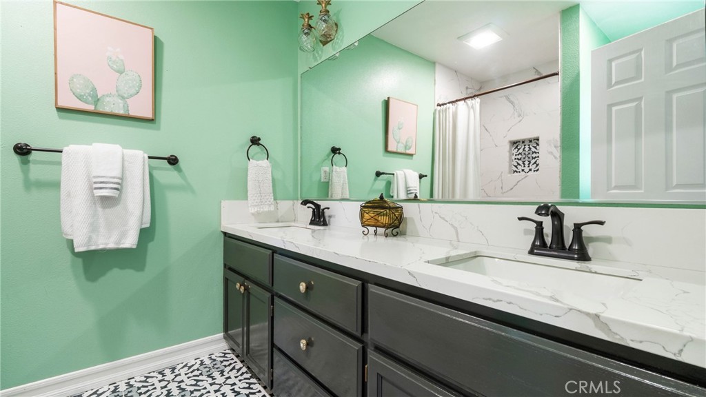 Bathroom with a dark double vanity, veined white countertop, mint-green walls, and patterned tile floor.