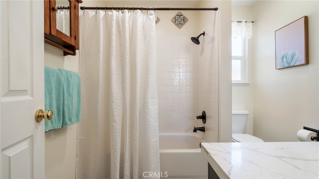 Bathroom with a curtained tub and shower, turquoise towels, and a marble-look vanity.