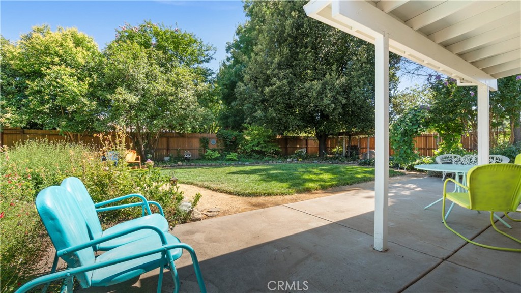 Covered backyard patio with colorful chairs overlooking a lawn and mature trees.