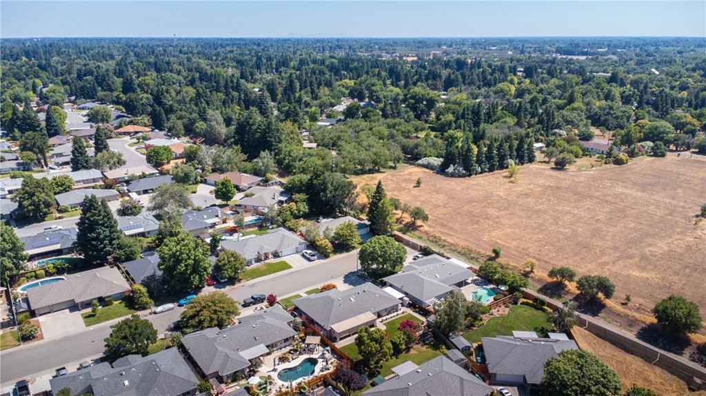 Aerial view of homes and backyard pools beside a large dry field.