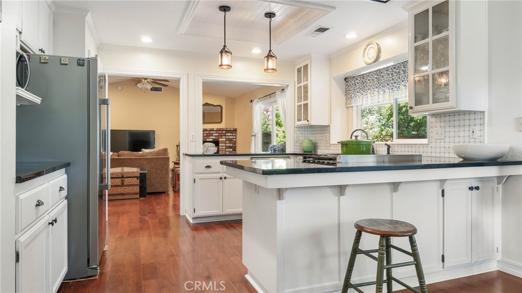 Bright white kitchen with a black island, pendant lights, and an opening to the living room.