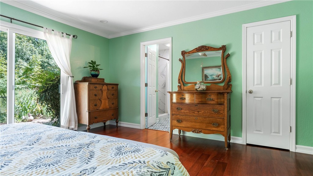 Mint-green bedroom with antique wooden dressers and a sliding glass door overlooking a leafy garden.