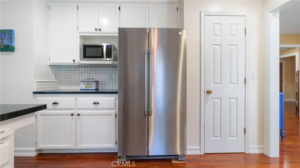 Kitchen with white cabinetry, stainless steel appliances, a tiled backsplash, and hardwood floors.