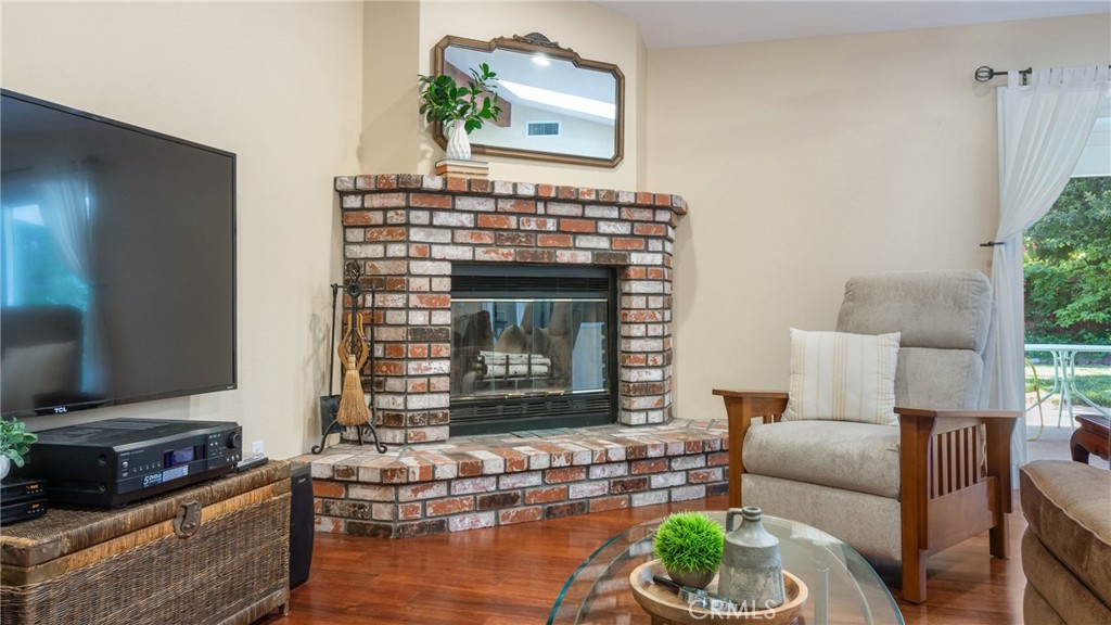 Living room with a brick fireplace, hardwood floors, and a curtained glass door to the patio.