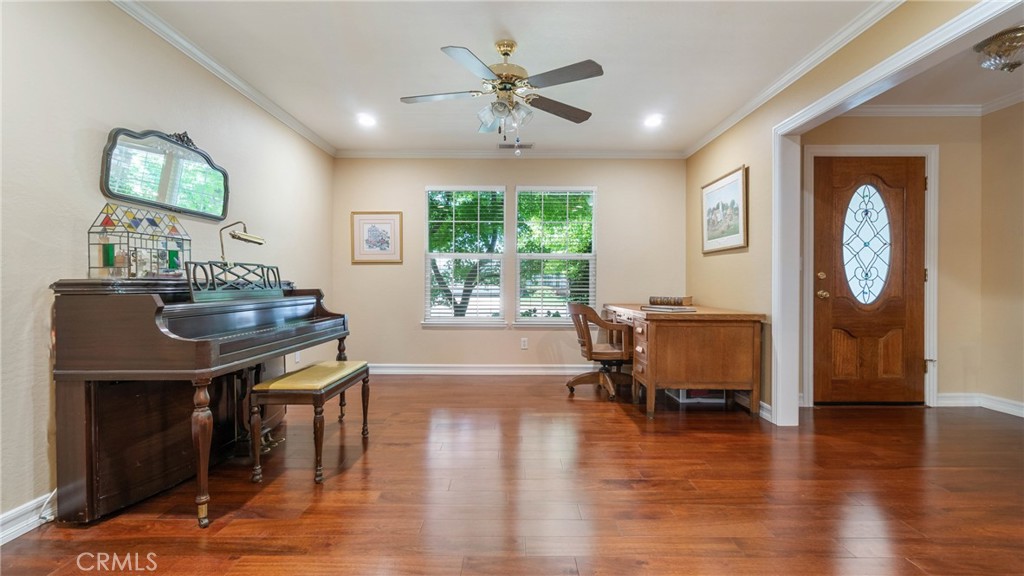 Furnished room with an upright piano, wooden desk, hardwood floors, and a decorative-glass entry door.