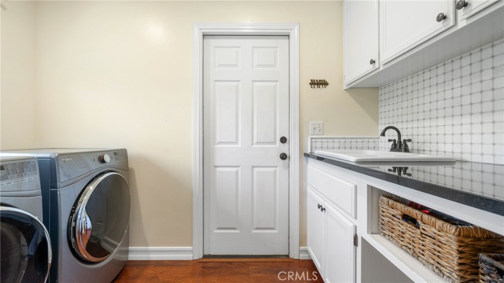 Laundry room with front-loading washer and dryer beside a built-in sink and cabinets.