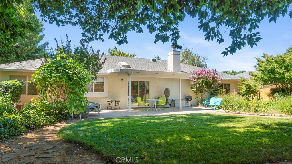 Rear of a single-story home with a covered patio and lawn framed by mature trees.