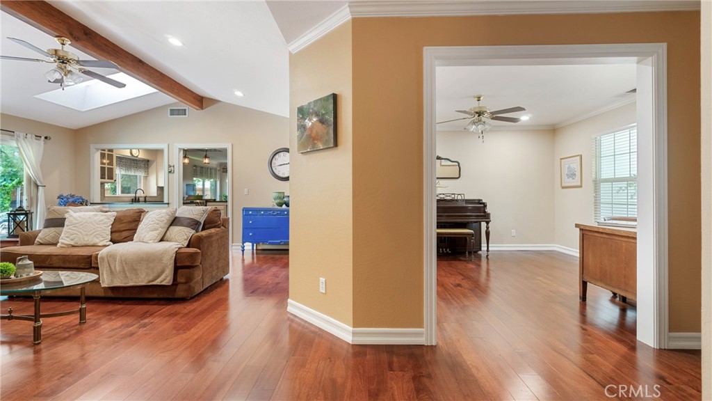 Living room with a brown sectional and wood floors, opening to a room with a piano.