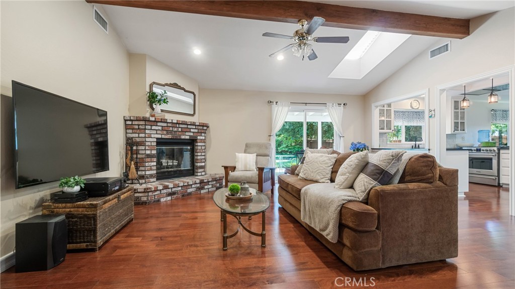Living room with brick fireplace, wall-mounted television, brown sectional, and reddish hardwood floors.