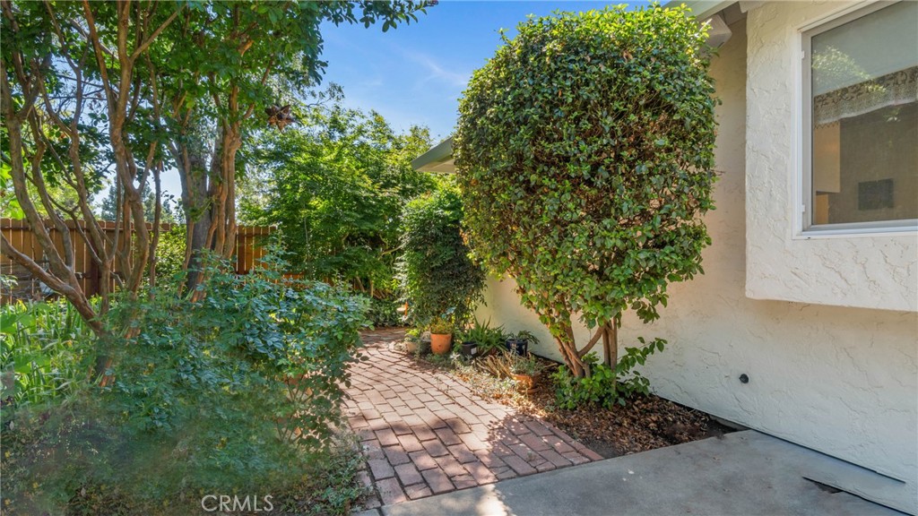 Brick walkway curves through landscaped garden beside a light stucco home.