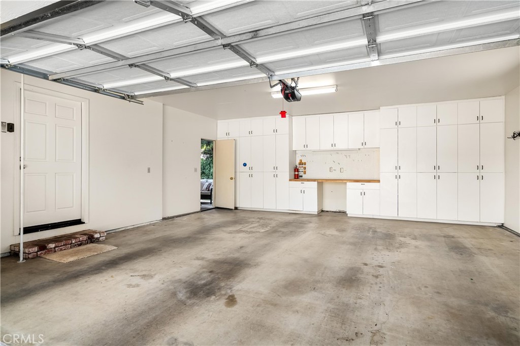 Empty garage with white storage cabinets, a workbench, and a raised garage door.