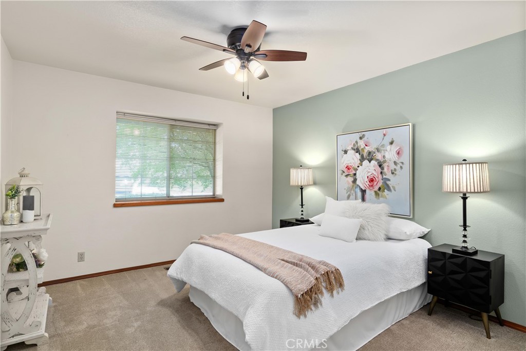 Staged bedroom with a white bed, sage green accent wall, floral artwork, and ceiling fan.