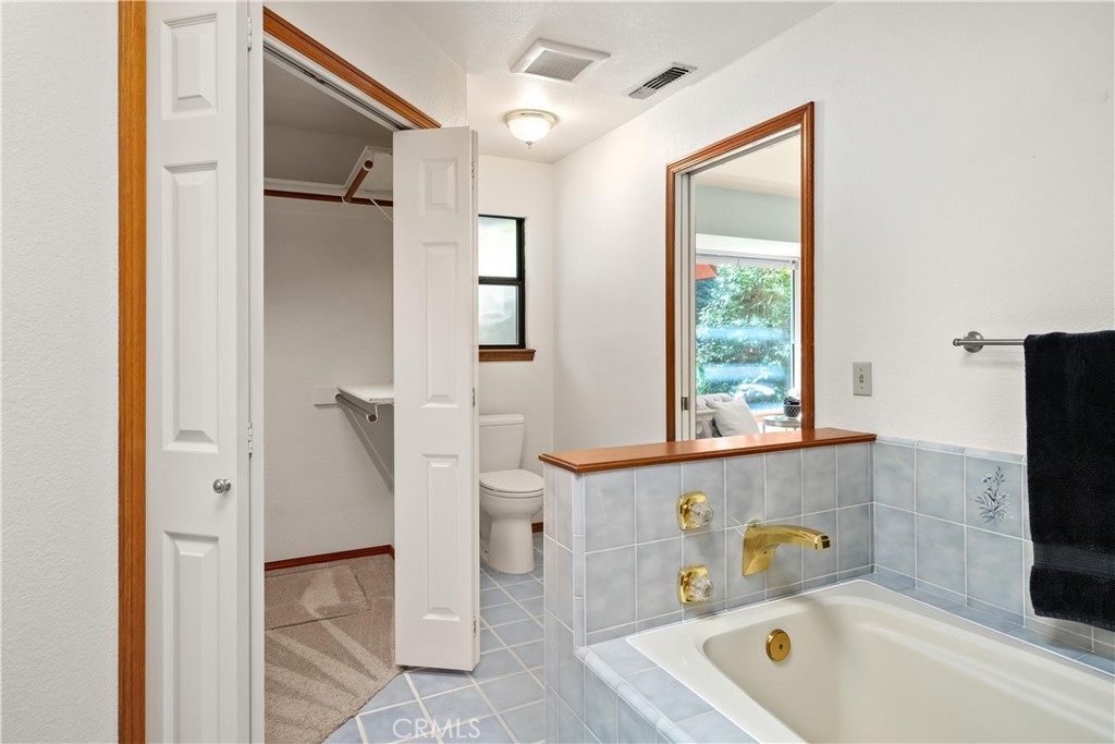 Bathroom with a pale blue tiled bathtub surround, gold fixtures, and an open closet.