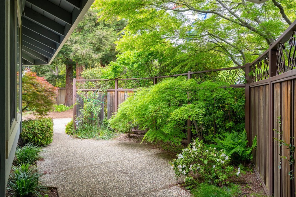 Landscaped side yard with a pebble walkway, leafy shrubs, and a decorative wood-and-metal fence.