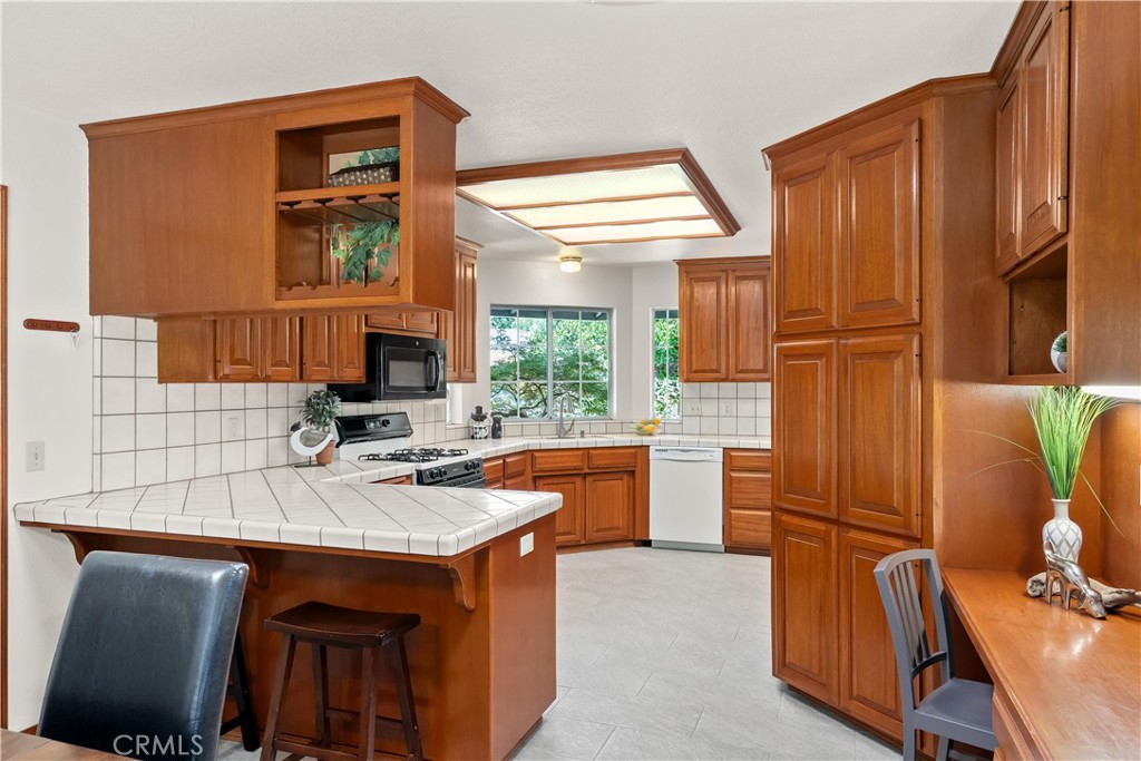 Kitchen with warm wood cabinets, tiled breakfast bar, gas range, and windows overlooking greenery.