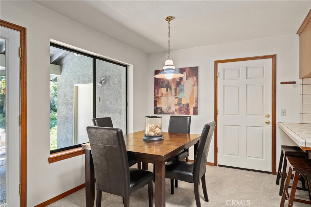 Dining area with a wood table, dark chairs, pendant light, and large window.