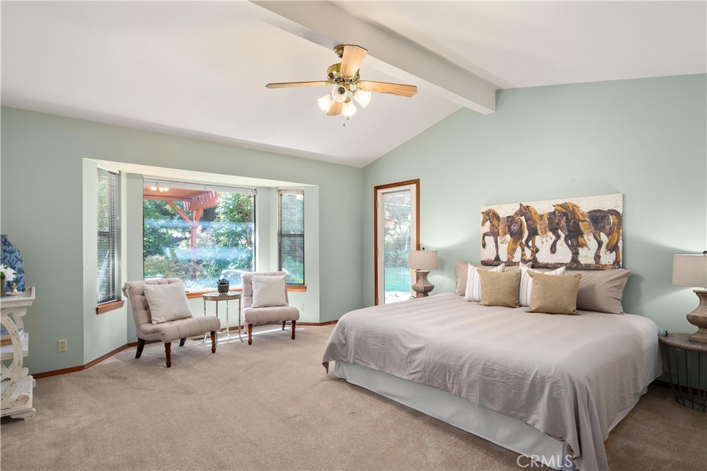 Bedroom with a large bed, vaulted ceiling, and window seating nook overlooking greenery.